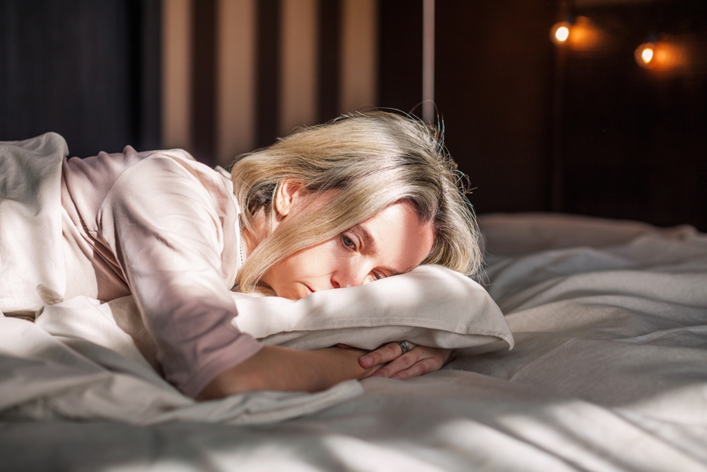A depressed woman laying in bed who has menopause symptoms of tiredness and lethargy